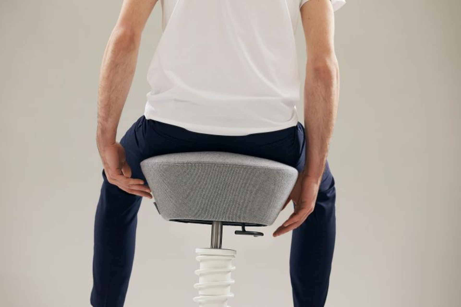 Mann sitzt auf einem grauen Swopper Hocker mit Rollen, ergonomischer Bürostuhl.