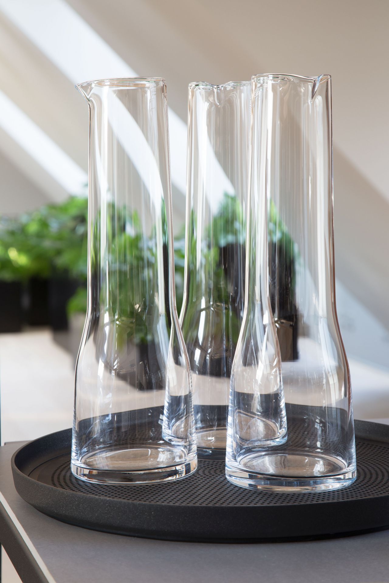 Drei leere, transparente Glaskaraffen auf einem schwarzen Vipp Tablett, minimalistisches Design für den Esstisch.