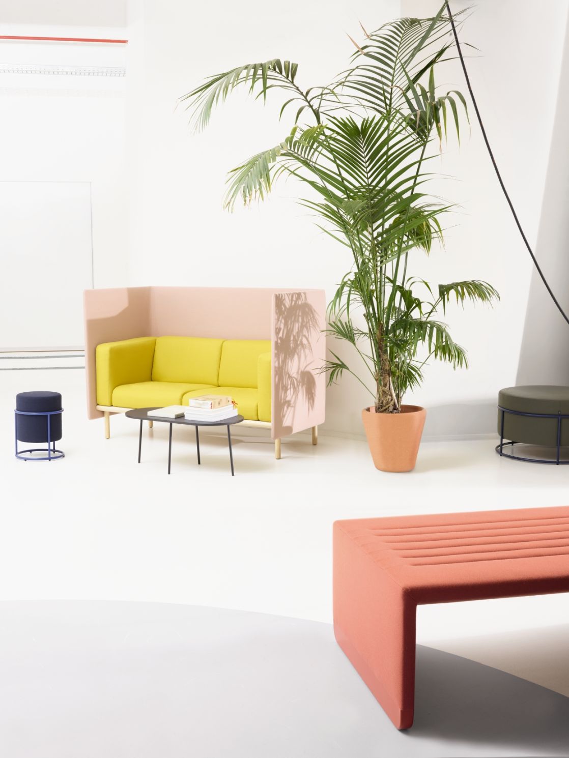 Helles Interieur mit Cor Floater 2-Sitzer Sofa in Gelb und Rosa, ergänzt durch Beistelltisch, Hocker und Zimmerpflanze.