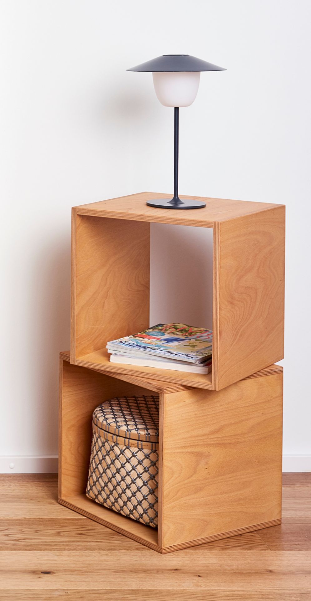 Tojo Cube Nachttisch aus Holz, gestapelt, mit Lampe, Zeitschriften und Korb im minimalistischen Schlafzimmer.