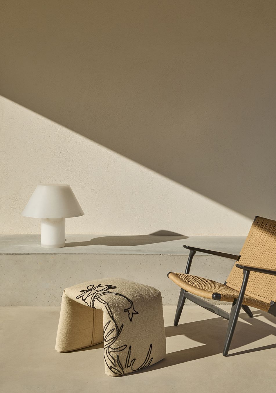 Beige Nanimarquina Bank "Folded Flower" mit floraler Stickerei, Lampe und Sessel im minimalistischen Interieur.