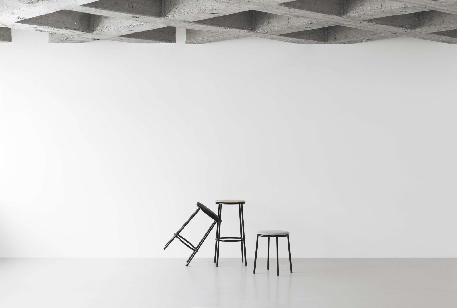 Circa Barhocker von Normann Copenhagen, zwei Barstühle mit schwarzem Gestell und hellem Sitz, einer umgekippt.