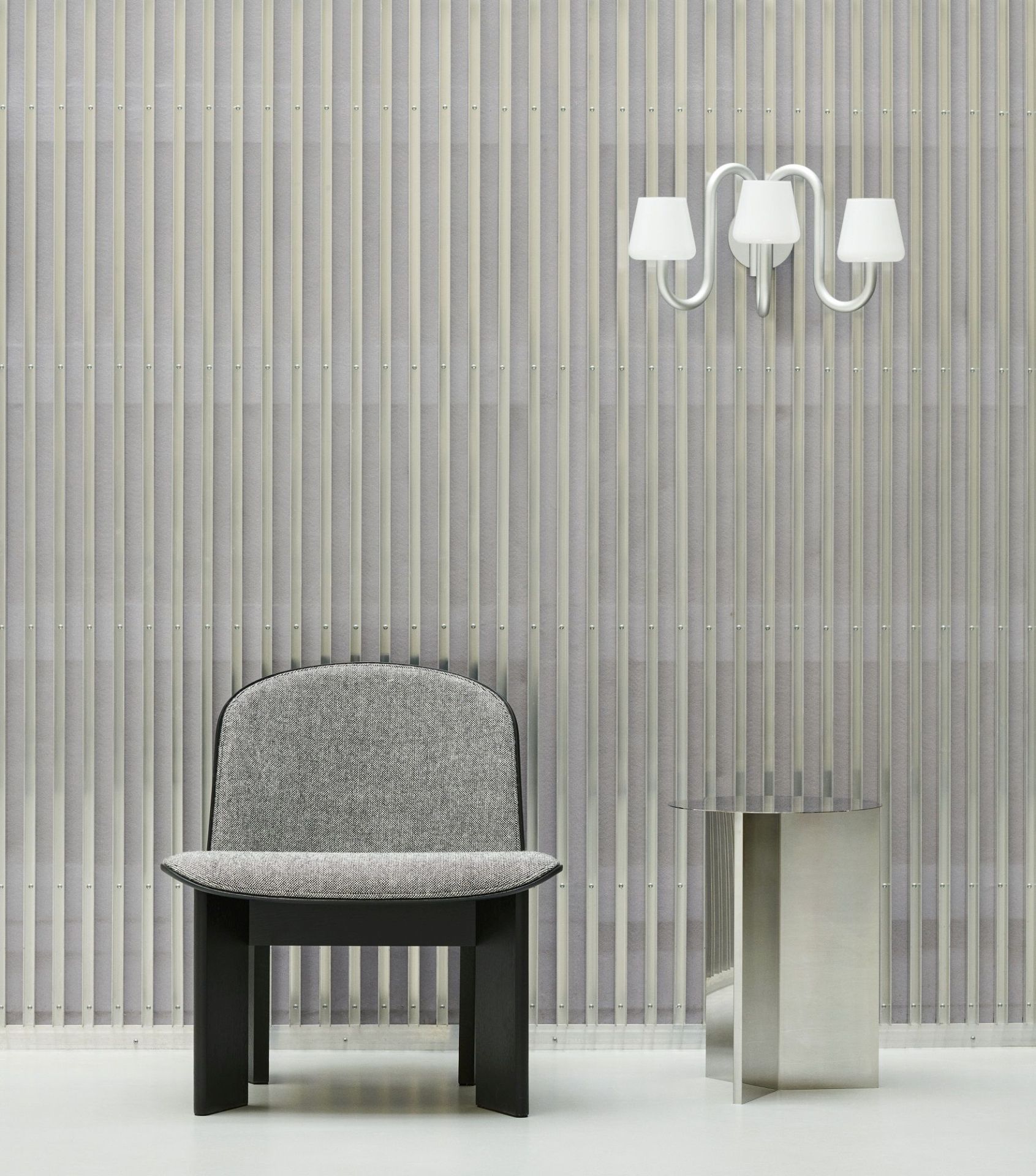 Hay Slit Table Round High Beistelltisch aus poliertem Edelstahl neben einem grauen Sessel und einer Lampe.