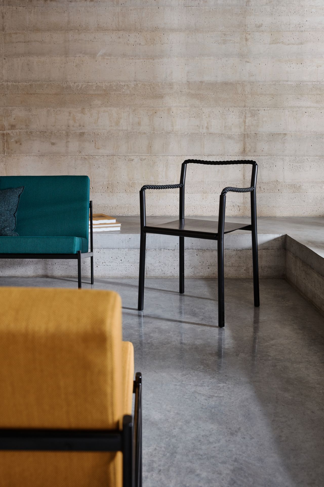 Artek Rope Chair Stuhl in Schwarz mit geflochtener Seil-Optik vor einer Betonwand.