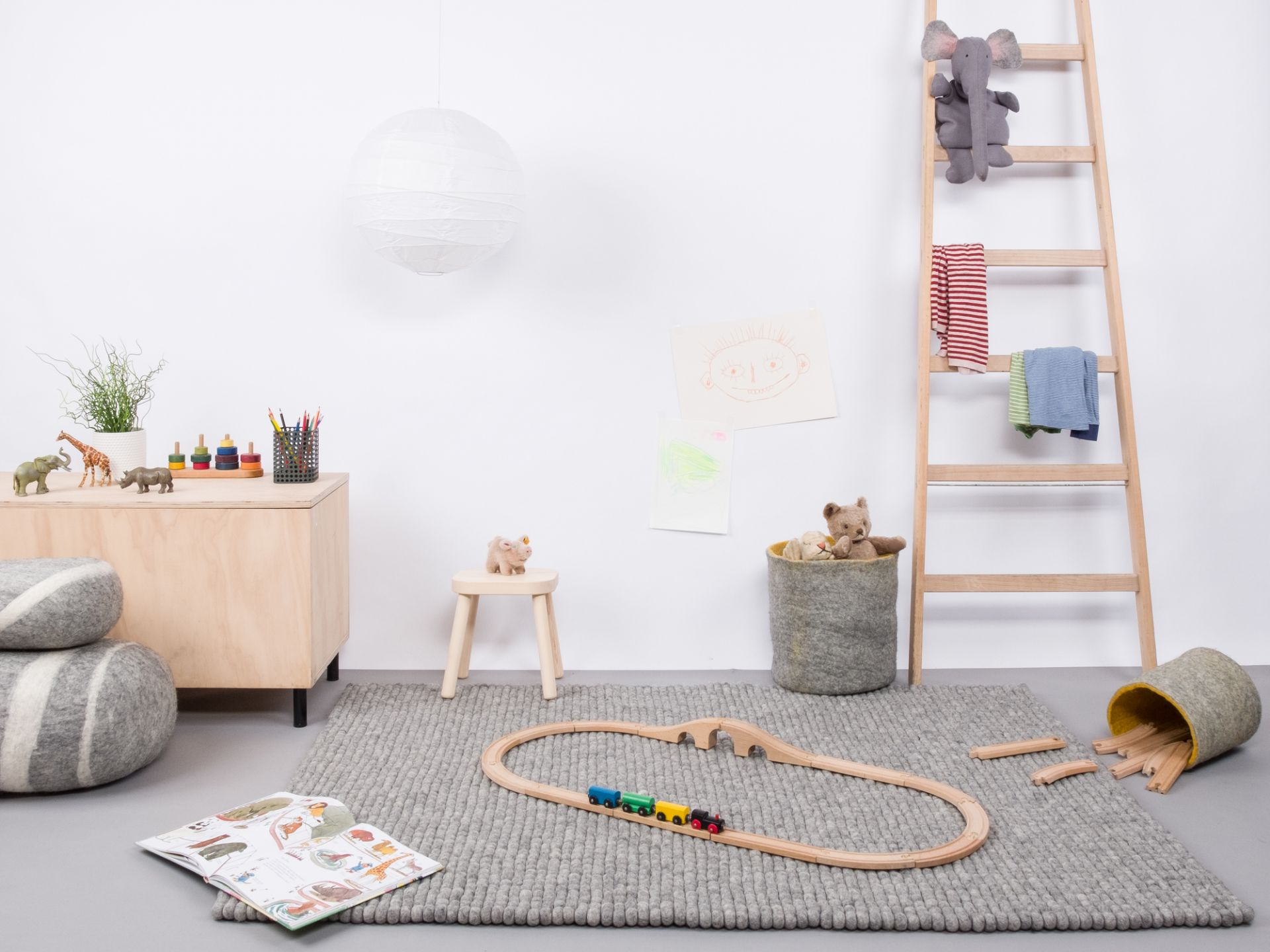 Grauer myfelt Filzkugel Teppich 120x170 cm im Kinderzimmer mit Spielzeug und Holzeisenbahn.