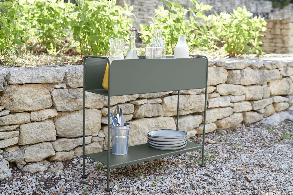 Picolino Übertopf von Fermob im Outdoor-Bereich: Metallgestell mit Pflanzen und Geschirr vor Steinmauer.
