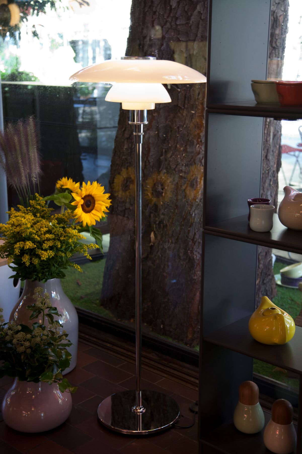 Moderne Stehlampe mit Lampenschirm in Weiß und Chromfuß, neben Blumenvasen und Dekoration.