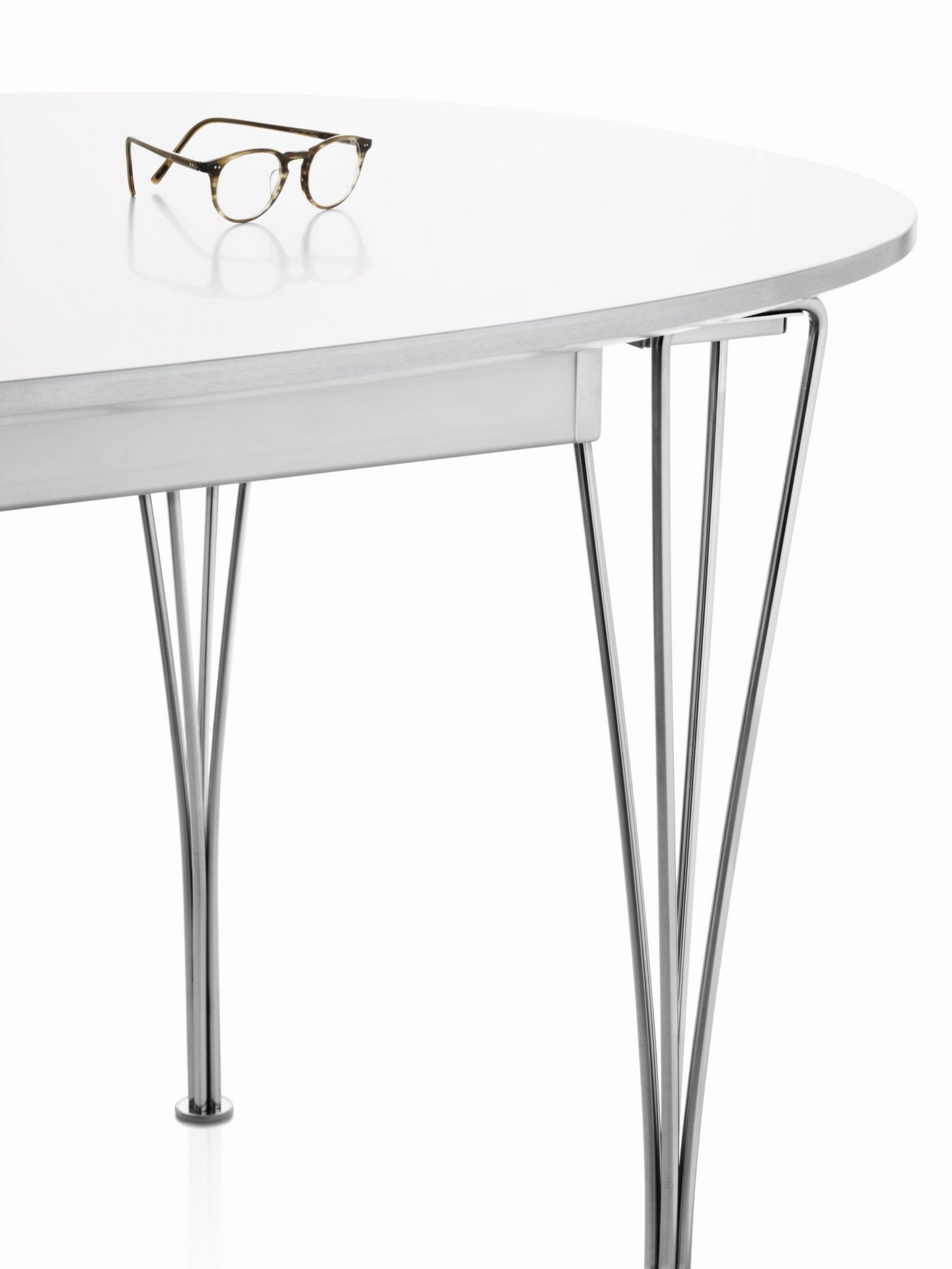 Detailaufnahme des Fritz Hansen Super Elliptisch Tisches mit weißer Tischplatte und verchromten Beinen, darauf eine Brille.