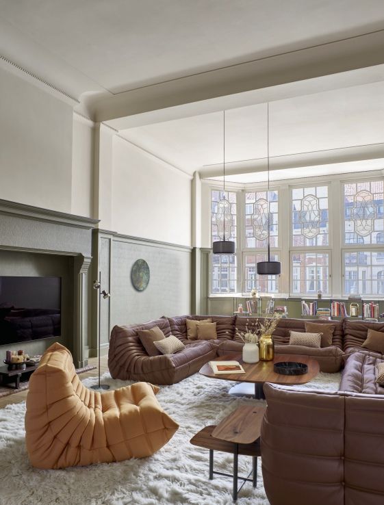 Wohnzimmer mit braunem Ligne Roset Togo Ledersofa, Sessel und Couchtisch auf einem weißen Teppich.