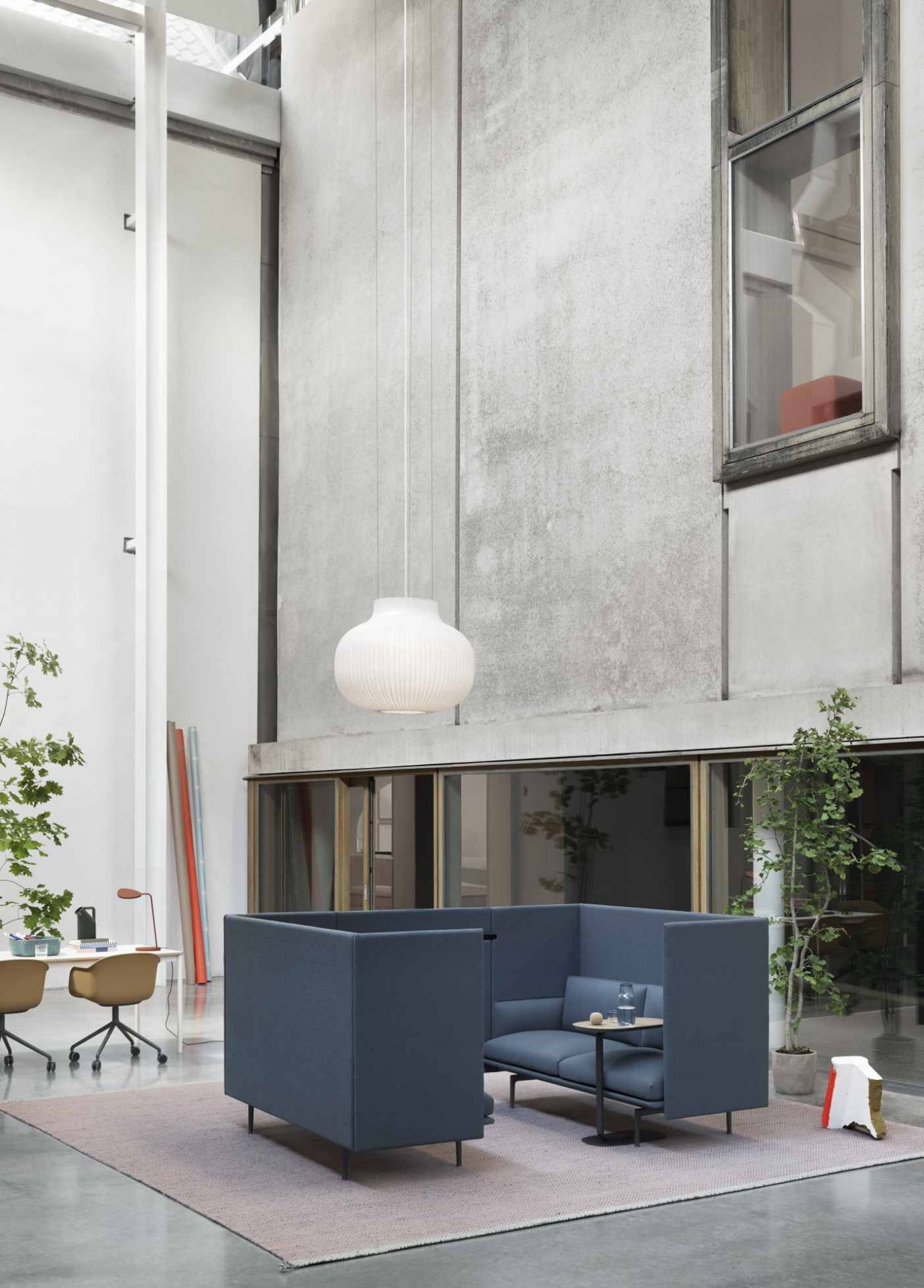 Helle, gerippte Muuto Strand Pendelleuchte über einer blauen Sitzecke in einem modernen Büro mit hohen Decken.