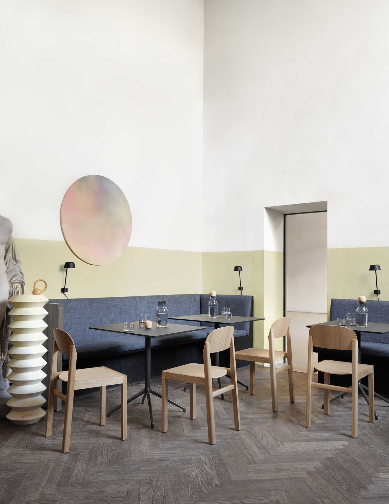 Innenaufnahme eines Cafés mit Muuto Still Cafe Tischen und Holzstühlen an einer blauen Sitzbank.