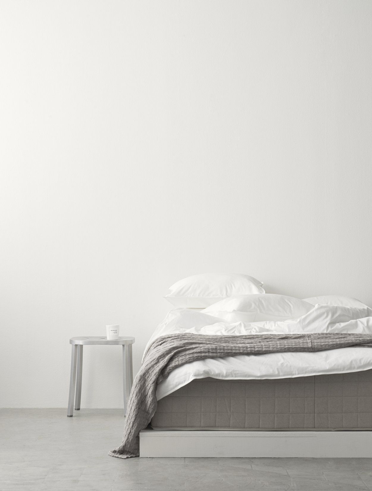Foto eines 1 Inch Emeco Hockers aus Aluminium neben einem Bett mit Decke.