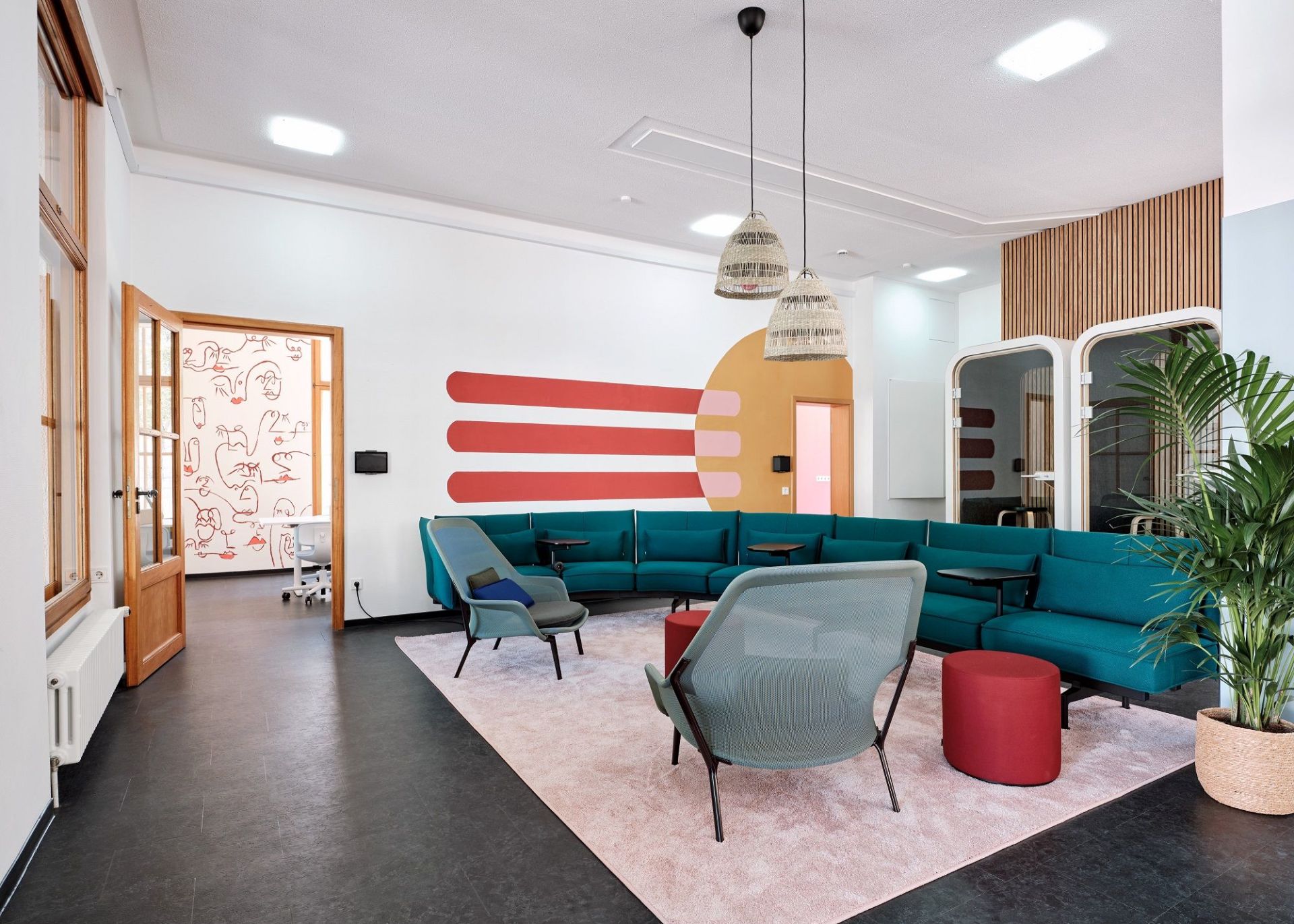 Einladender Bürobereich mit türkisfarbenem Modulsofa und zwei Slow Chair Sesseln von Vitra auf einem rosa Teppich.