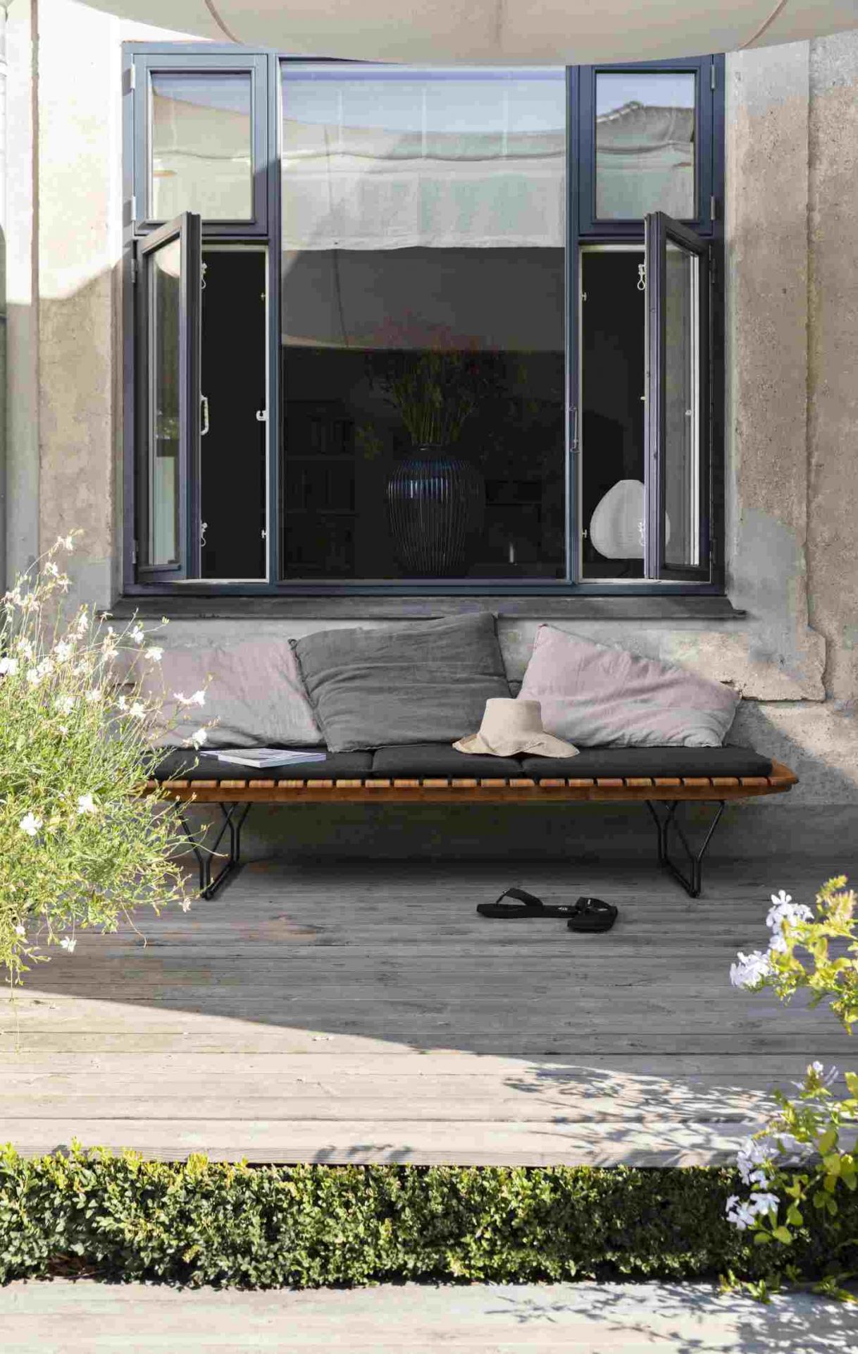 Houe Sonnenliege mit Molo Outdoor Kissen, grauer Bezug, hellrosa Zierkissen und Strohhut auf Terrasse.