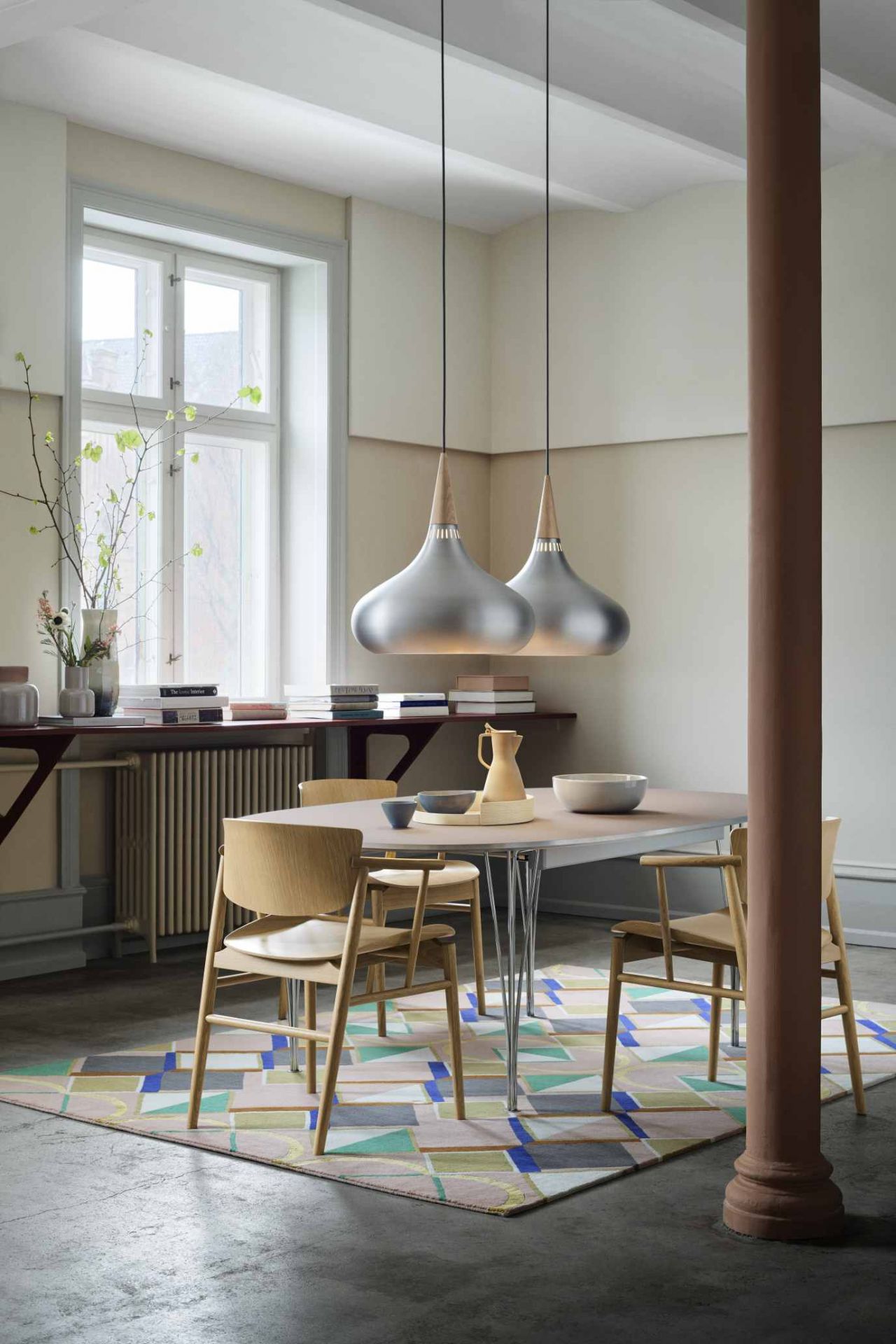 Fritz Hansen Super Elliptisch Ausziehtisch mit Holzstühlen und zwei Pendelleuchten in einem hellen Esszimmer.