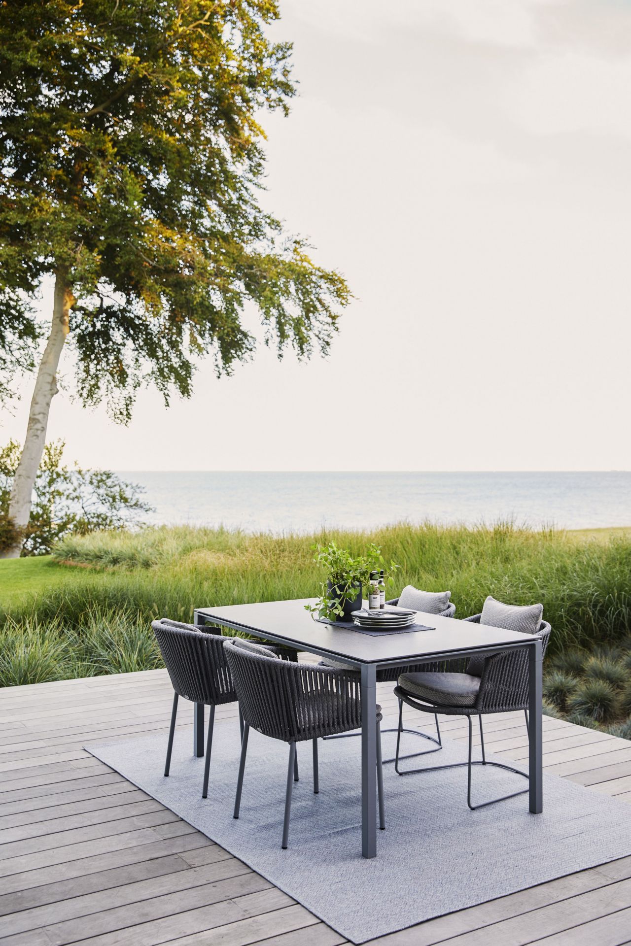 Cane-Line Outdoor Teppich unter Esstisch mit Stühlen auf Holzterrasse am Meer. Wetterfester Teppich.