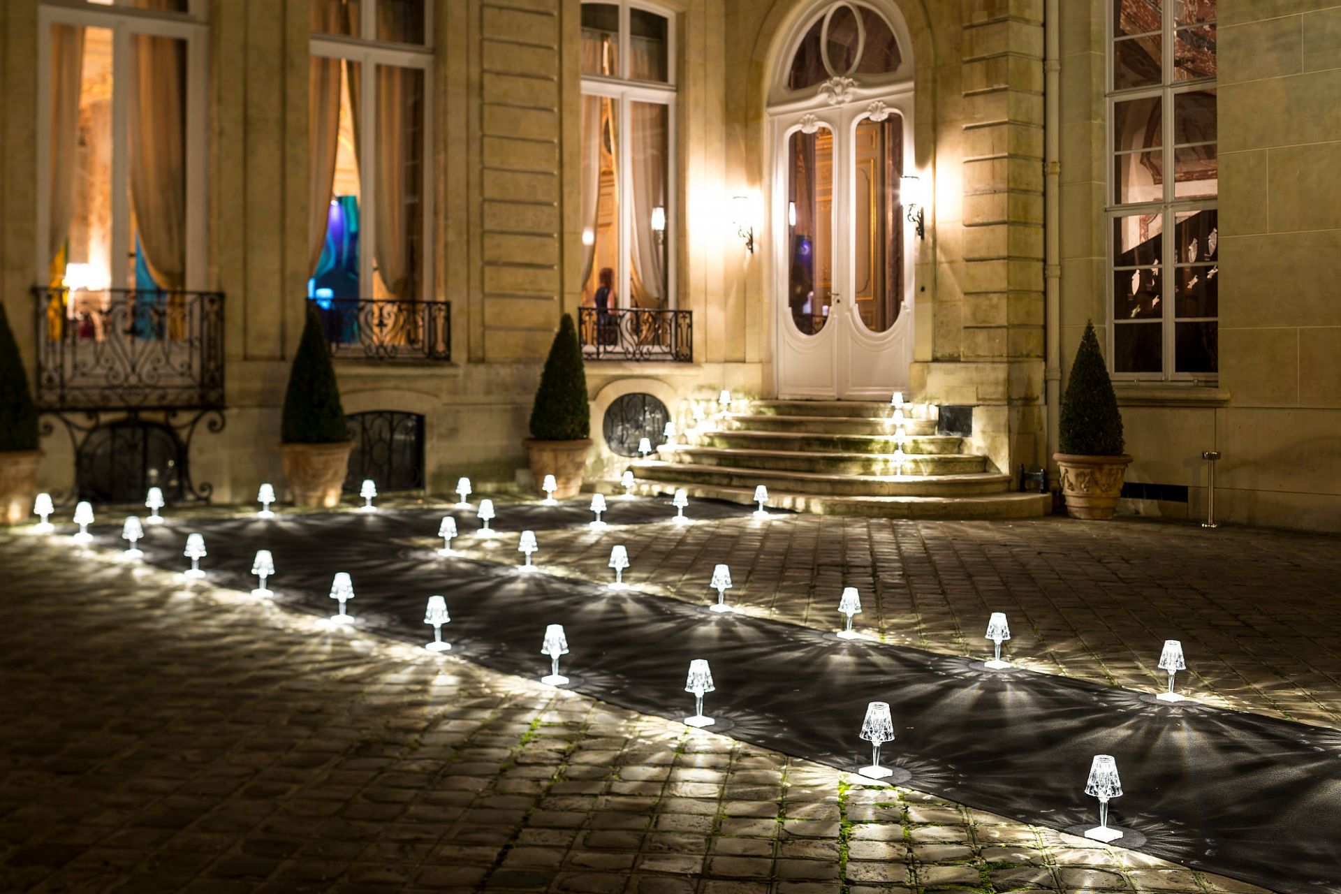 Battery Tischleuchte von Kartell, rauchfarben, beleuchtet einen Weg vor einem Gebäude. Dekorative LED Lampe.
