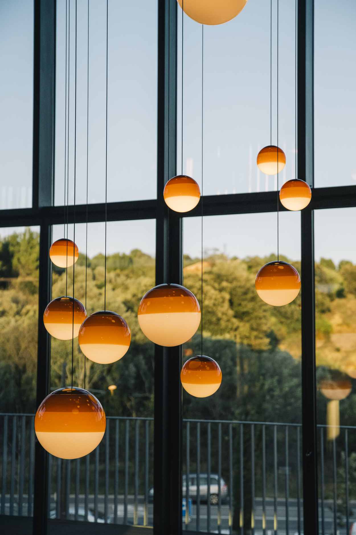 Mehrere Dipping Light Pendelleuchten in Bernstein vor einem Fenster mit Ausblick.