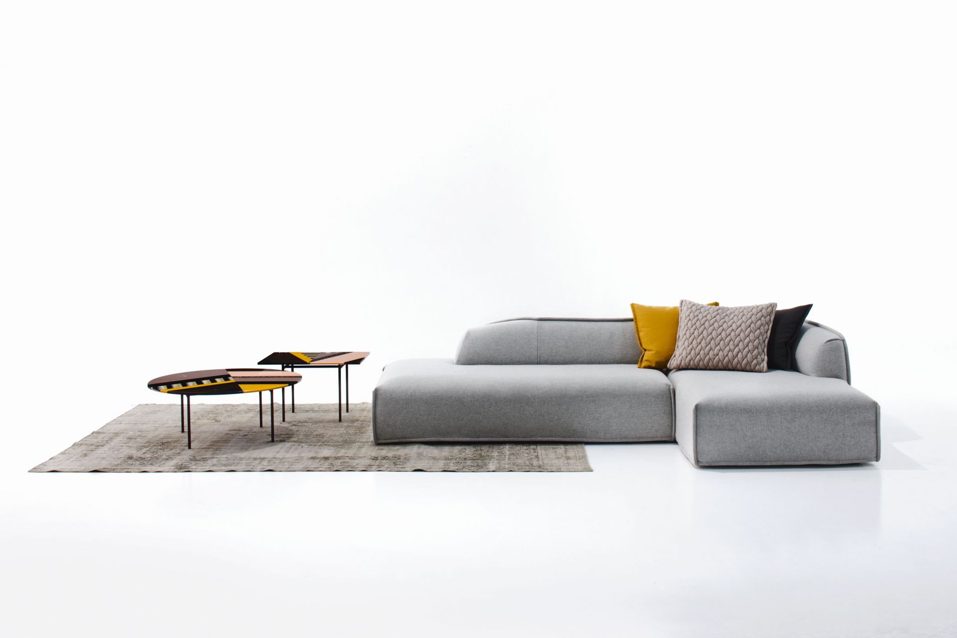 Fishbone Tisch von Moroso, gelb und braun, neben einem grauen Sofa auf einem Teppich.