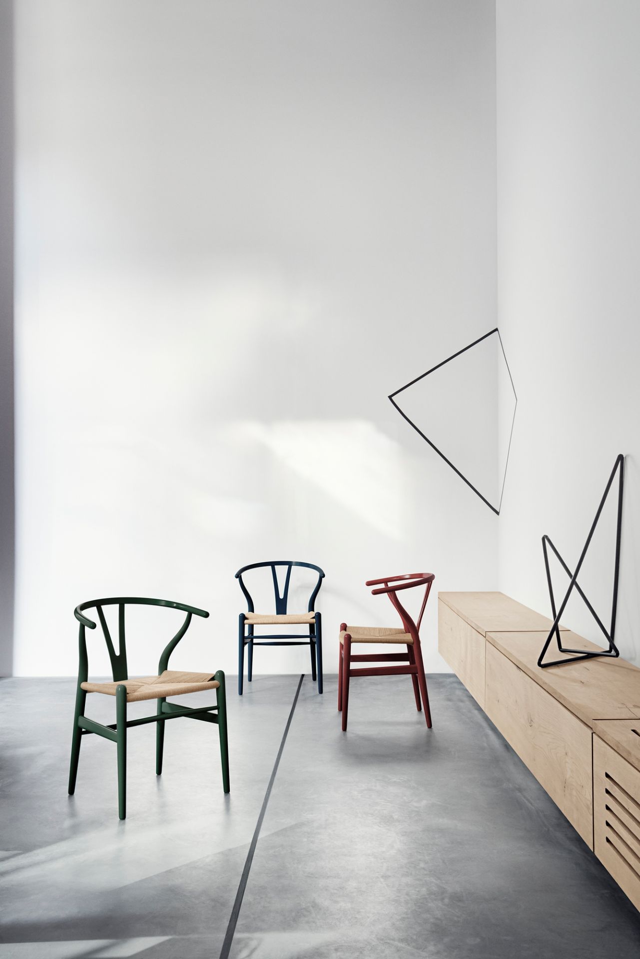 Drei CH24 Wishbone Stühle in Grün, Blau und Russet mit geflochtenen Sitzen in minimalistischem Interieur.