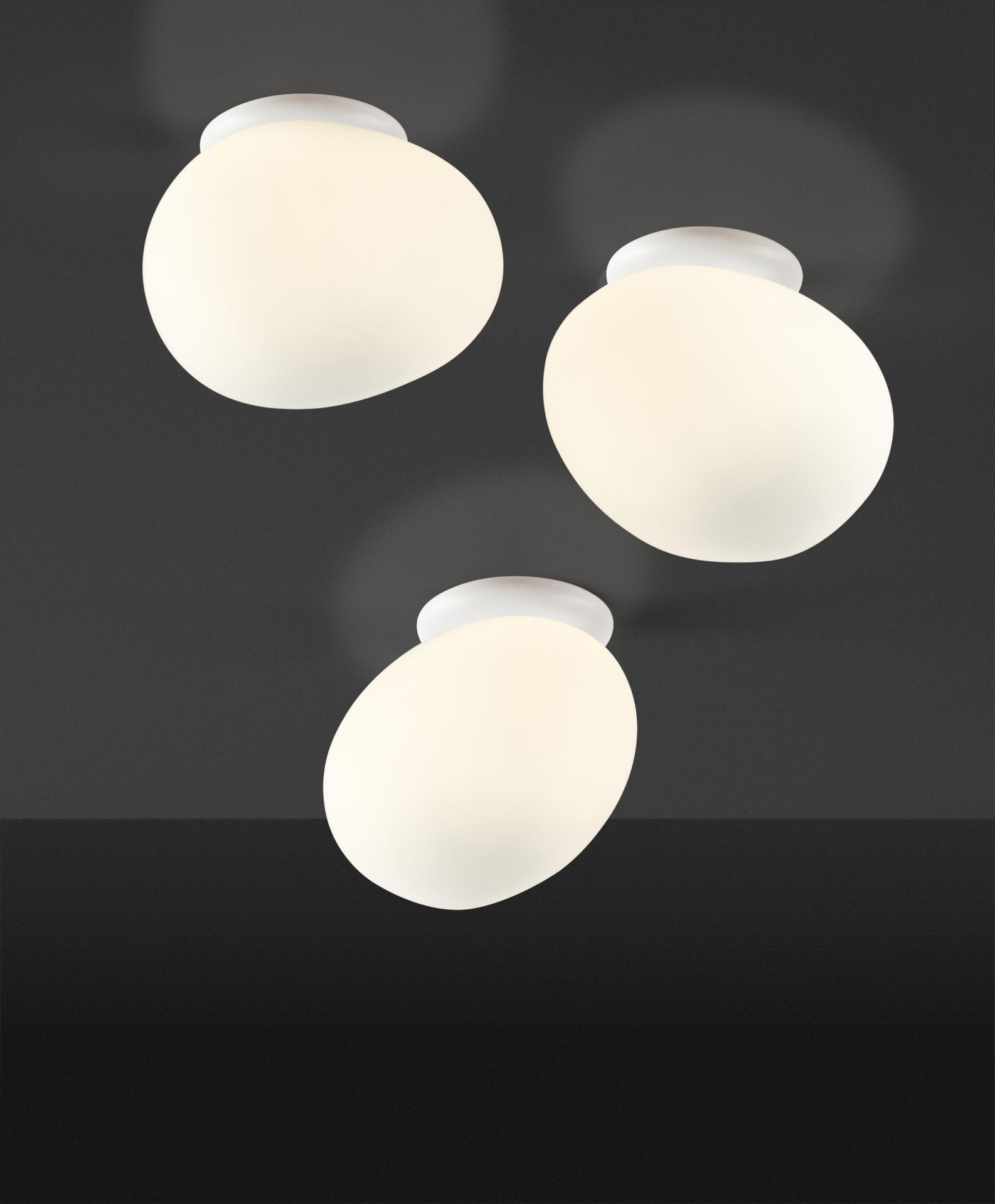 Drei weiße Gregg Deckenleuchten von Foscarini an einer dunklen Decke, modernes Design.