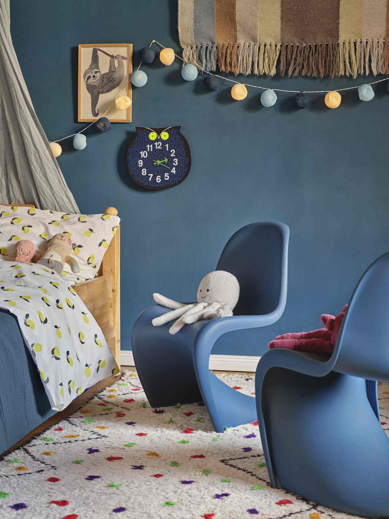Kinderzimmer mit Vitra Omar the Owl Wanduhr, blauen Stühlen und verspieltem Teppich für eine gemütliche Atmosphäre.