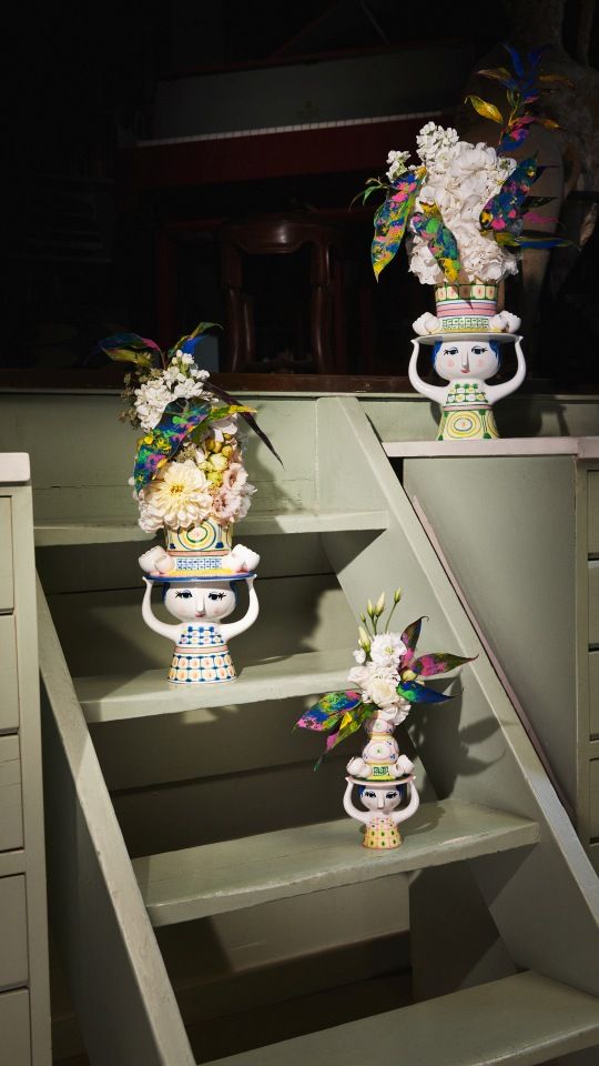 Drei Bjorn Wiinblad Lady with Hat Vasen auf einer grünen Treppe, gefüllt mit bunten Blumen.