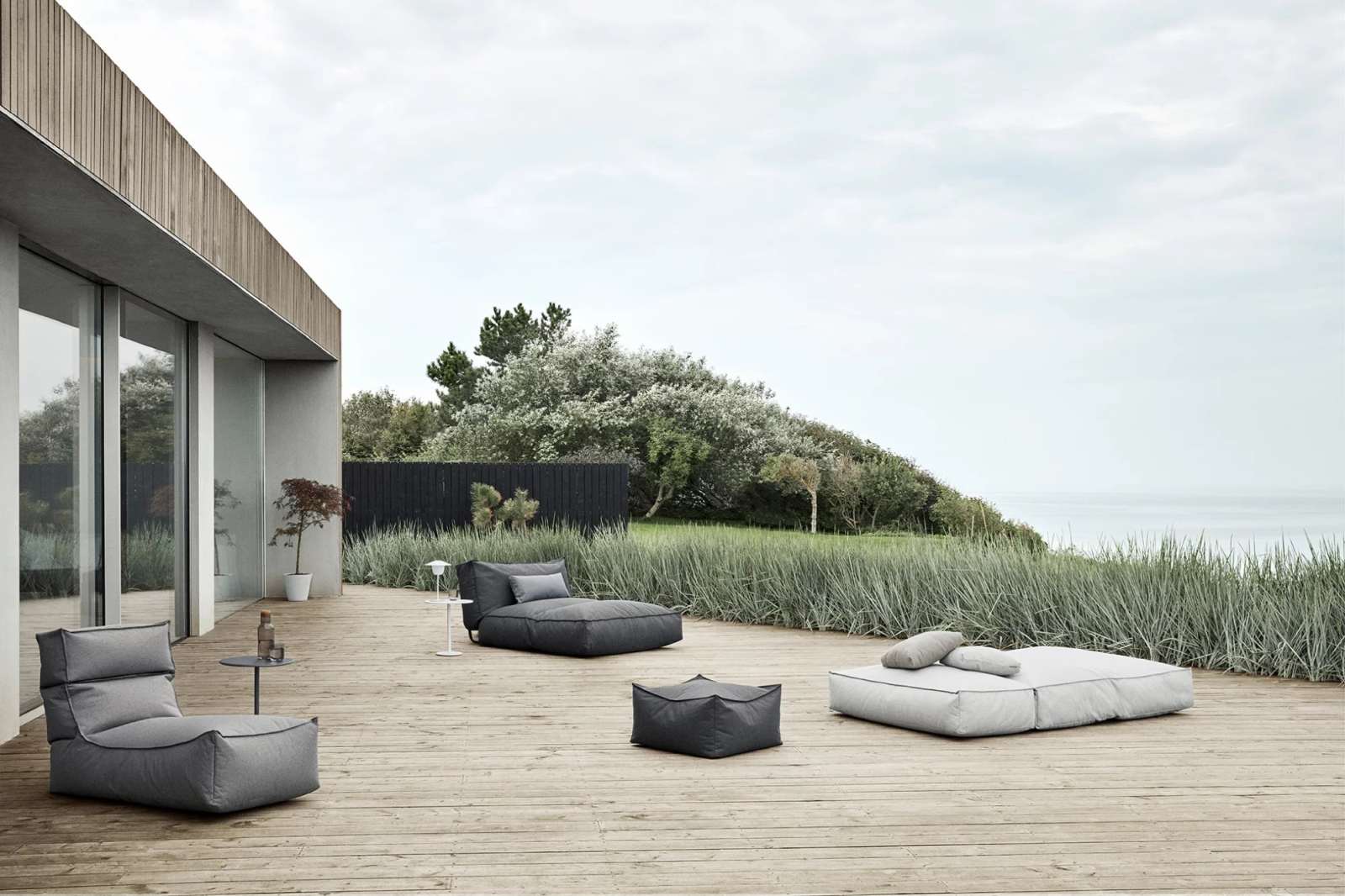 Blomus Stay Day Bed Outdoor Tagesbett auf Holzterrasse mit Garten und Meerblick.