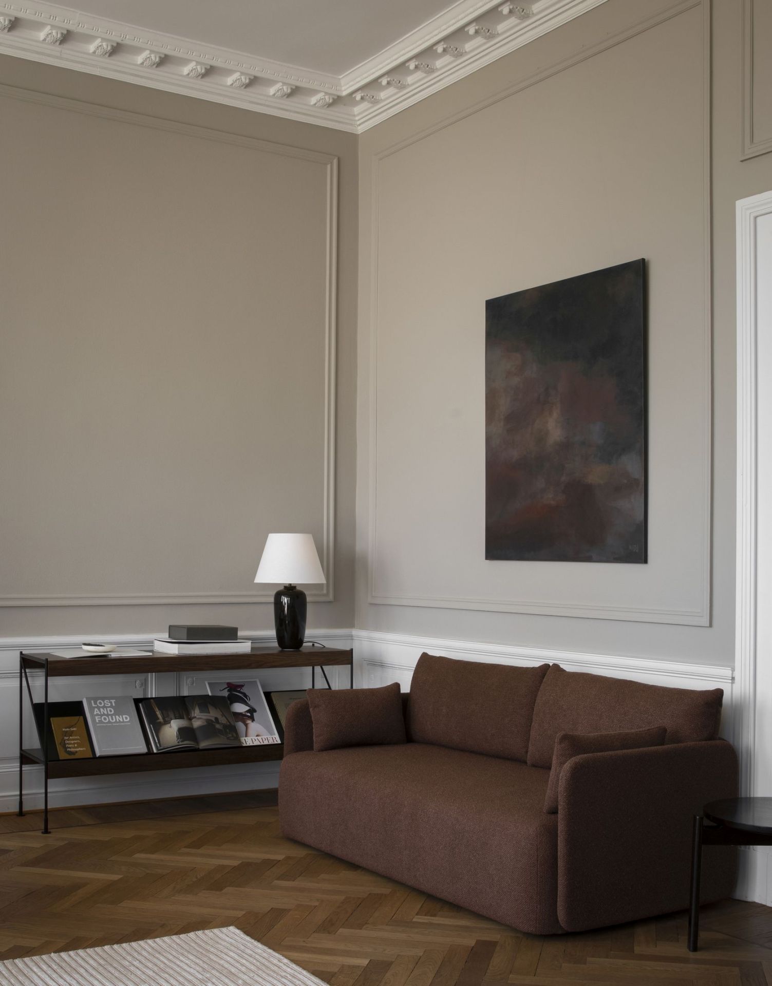 Wohnzimmer-Szene mit braunem Sofa und Audo Copenhagen Zet Storage System Regal mit Büchern und Lampe.