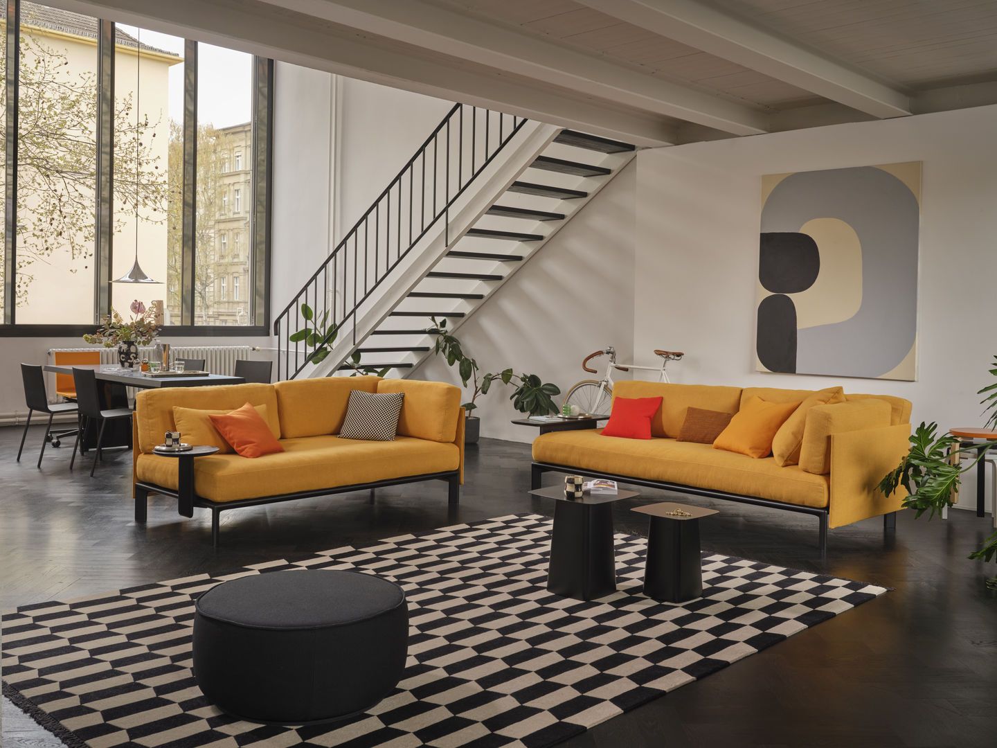 Wohnzimmer mit zwei gelben Vitra Anagram Sofas, verbunden durch Plattformverbinder, auf einem schwarz-weiß gemusterten Teppich.