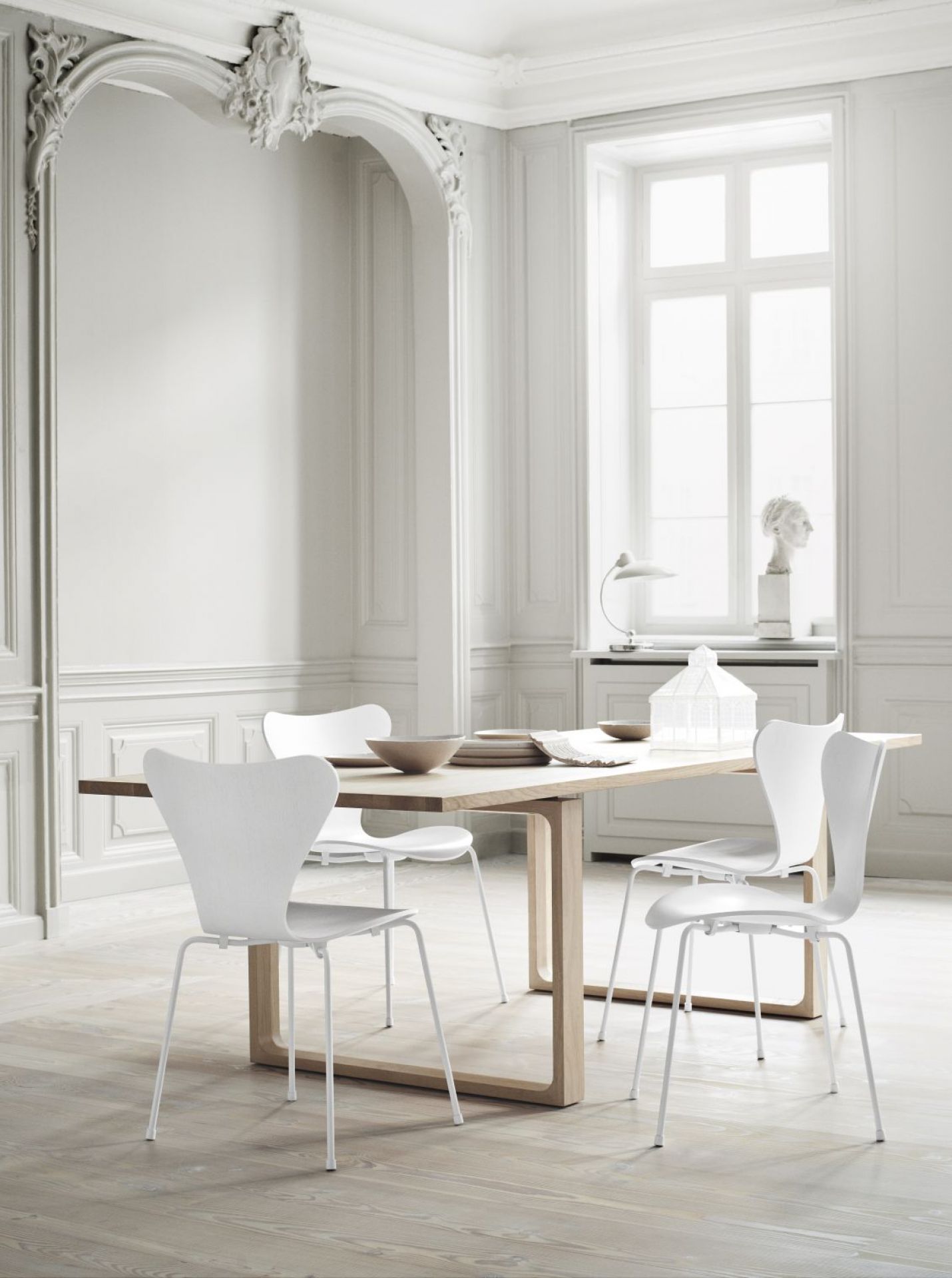 Heller Raum mit Fritz Hansen Essay Tisch aus Holz und weißen Stühlen, Essteller und Schalen.
