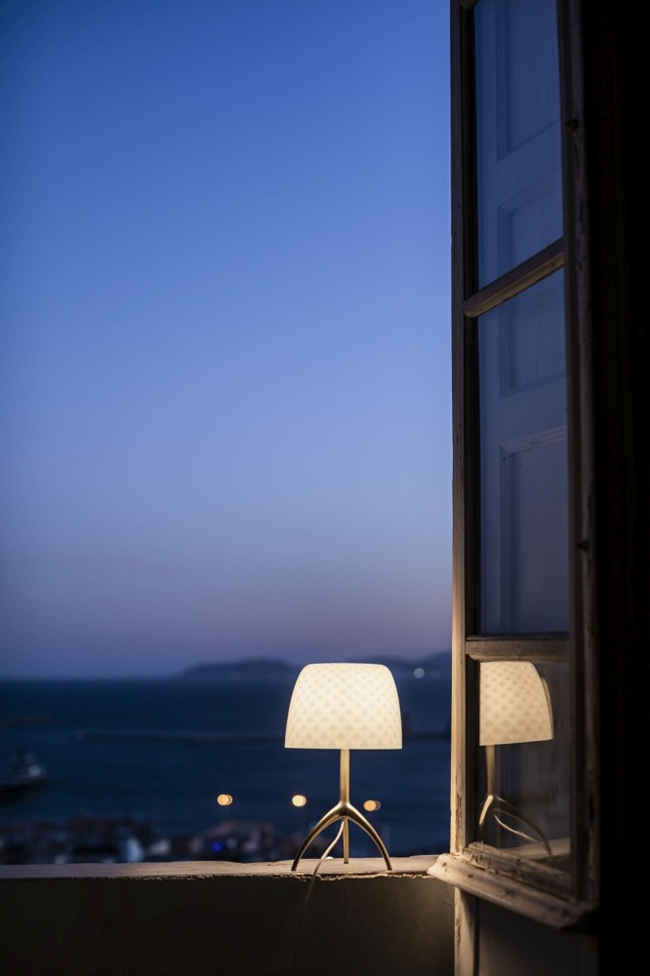 Lumiere Tischleuchte von Foscarini auf Fensterbank mit Meerblick, modernes Design für stimmungsvolle Beleuchtung.