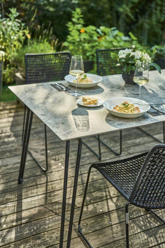 Slope Tisch von Weishäupl, graue Tischplatte, schwarzes Gestell, gedeckt mit Pasta und Wein im Garten.