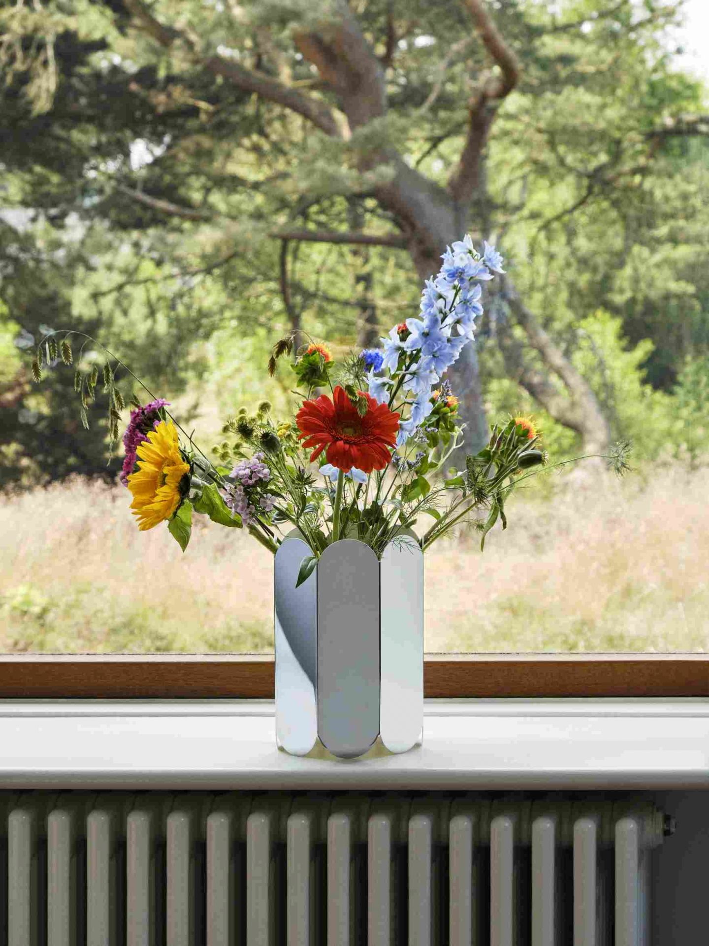 Nahaufnahme der Hay Arcs Vase L Mirror mit bunten Blumen auf einer Fensterbank.