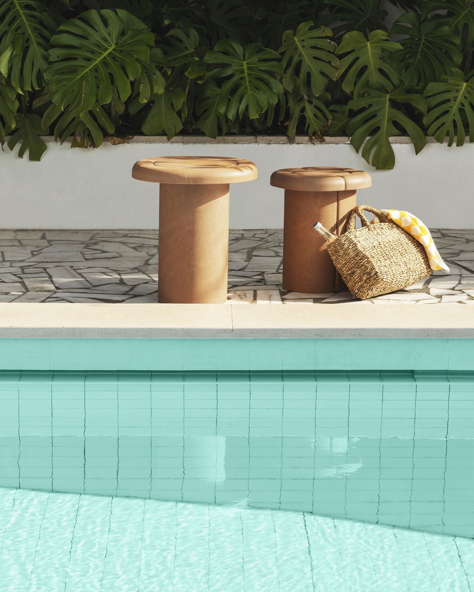 Zwei Alder Beistelltische in Terrakotta neben einem Pool, mit Strandtasche und Handtuch.