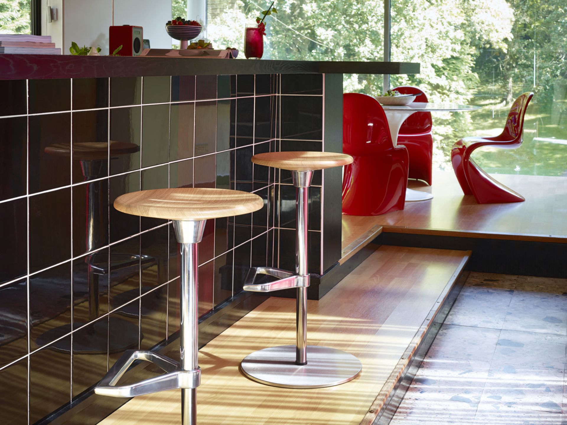Innenaufnahme mit zwei Barhockern und roten Panton Stühlen von Vitra im Hintergrund.