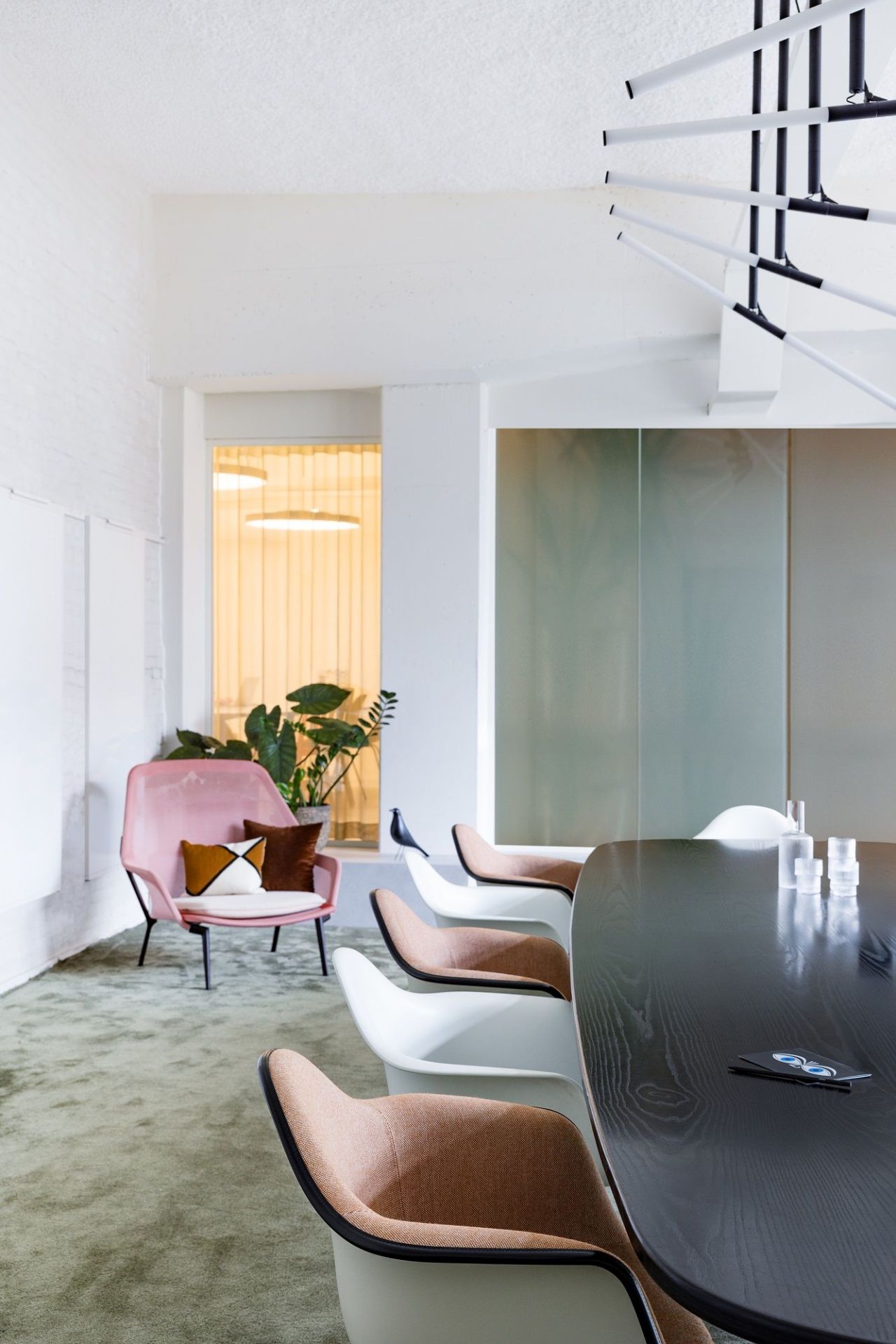 Innenaufnahme mit rosa Vitra Slow Chair Sessel, braunen und weißen Stühlen um einen dunklen Holztisch.