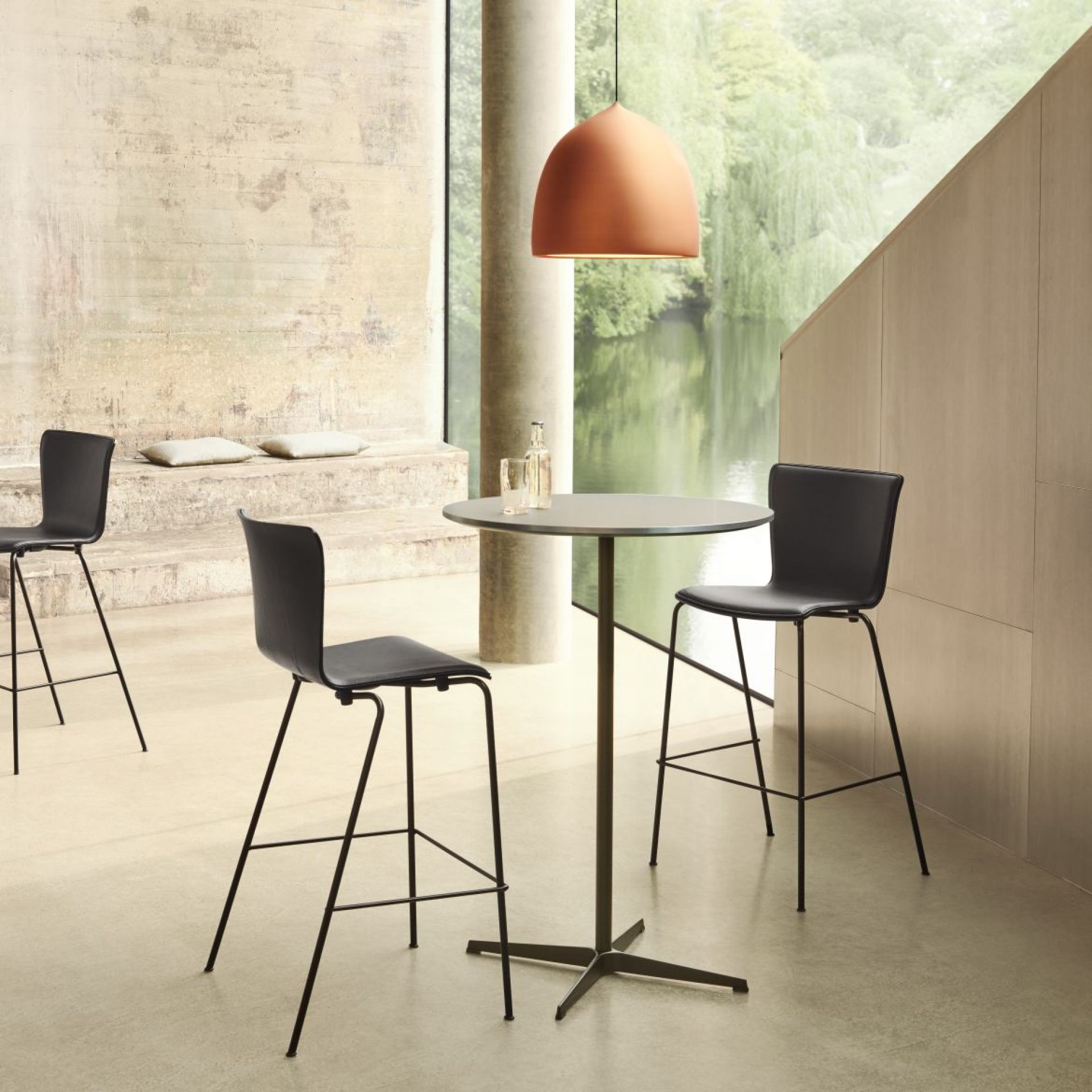 Innenaufnahme mit Fritz Hansen Stehtisch Zirkular, graue Tischplatte, schwarzes Gestell, kombiniert mit Barhockern und Pendelleuchte.