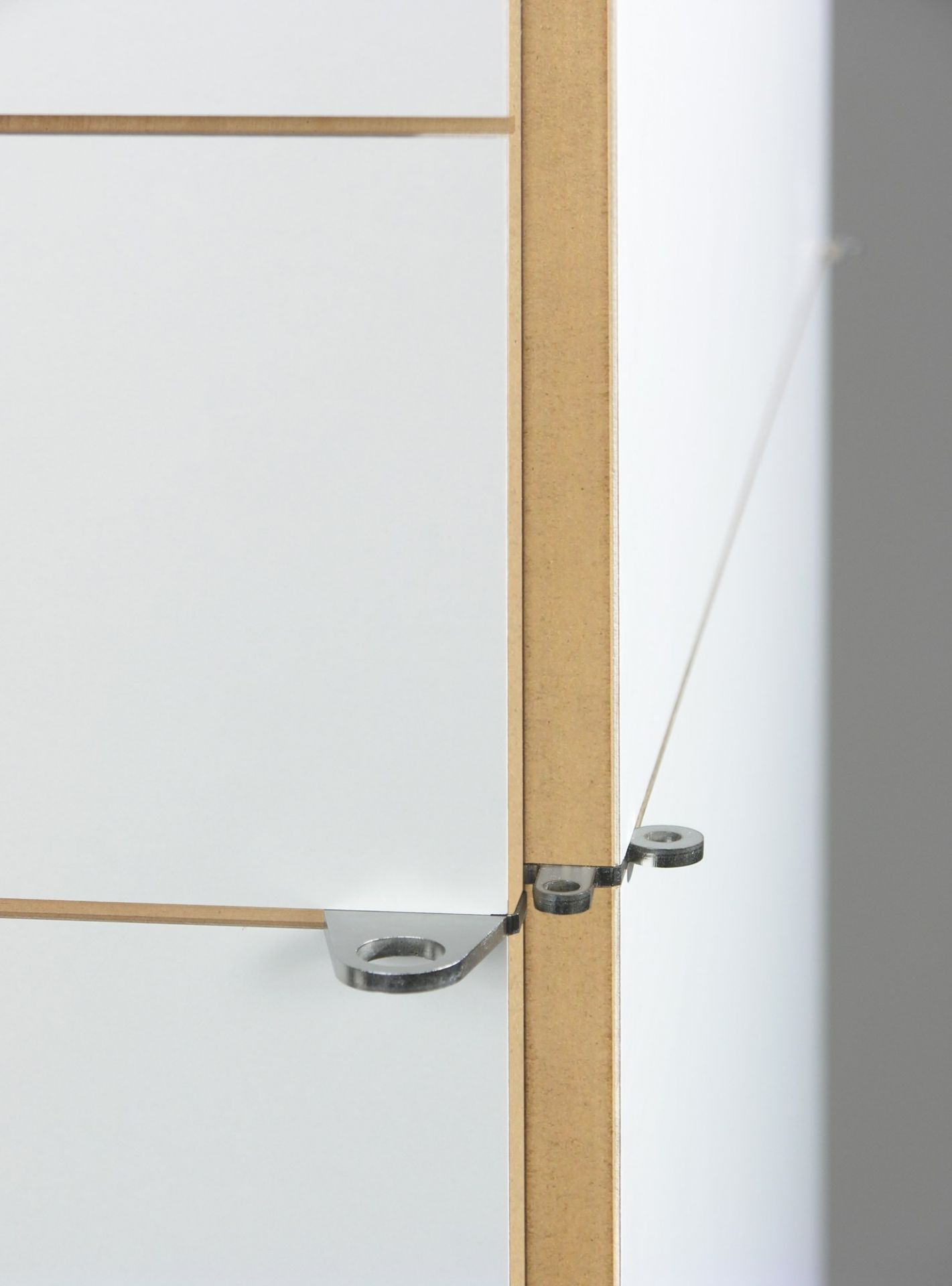 Detailaufnahme K1 Armoire von Nils Holger Moormann: Weiße Schranktür mit innovativer, metallener Aufhängung und Holzrahmen.