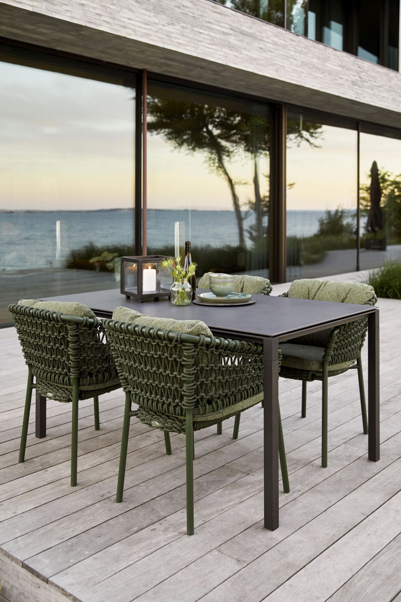 Ocean Lounge Stuhl von Cane-Line: Gartenmöbel-Set mit Esstisch und grünen Outdoor-Stühlen auf Holzterrasse.