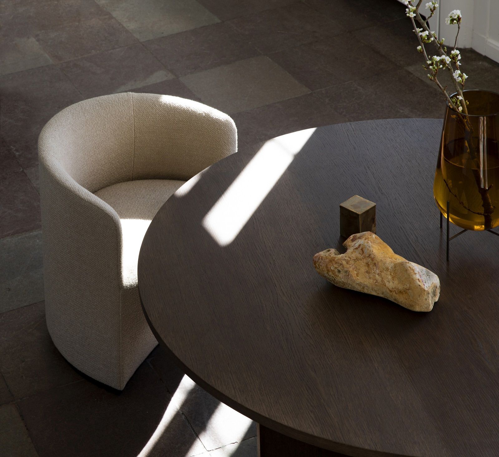 Audo Copenhagen Tearoom Lounge Chair Sessel in Beige neben einem dunklen Holztisch mit Dekoration.