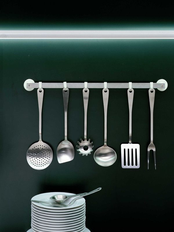 Alessi Küchenset mit Edelstahl-Küchenhelfern an einer Stange und gestapelten Tellern, modernes Küchendesign.