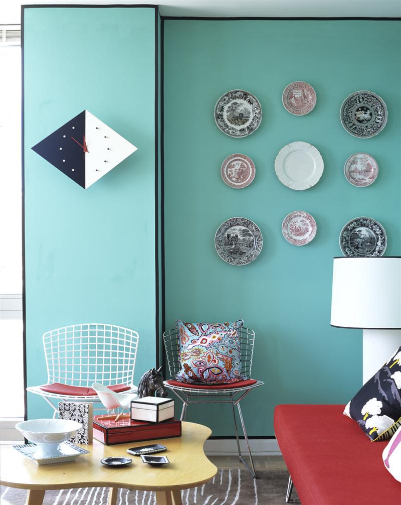 Zwei Bertoia Stühle mit roten Sitzkissen, einer mit buntem Kissen, im Wohnzimmer mit türkiser Wand.