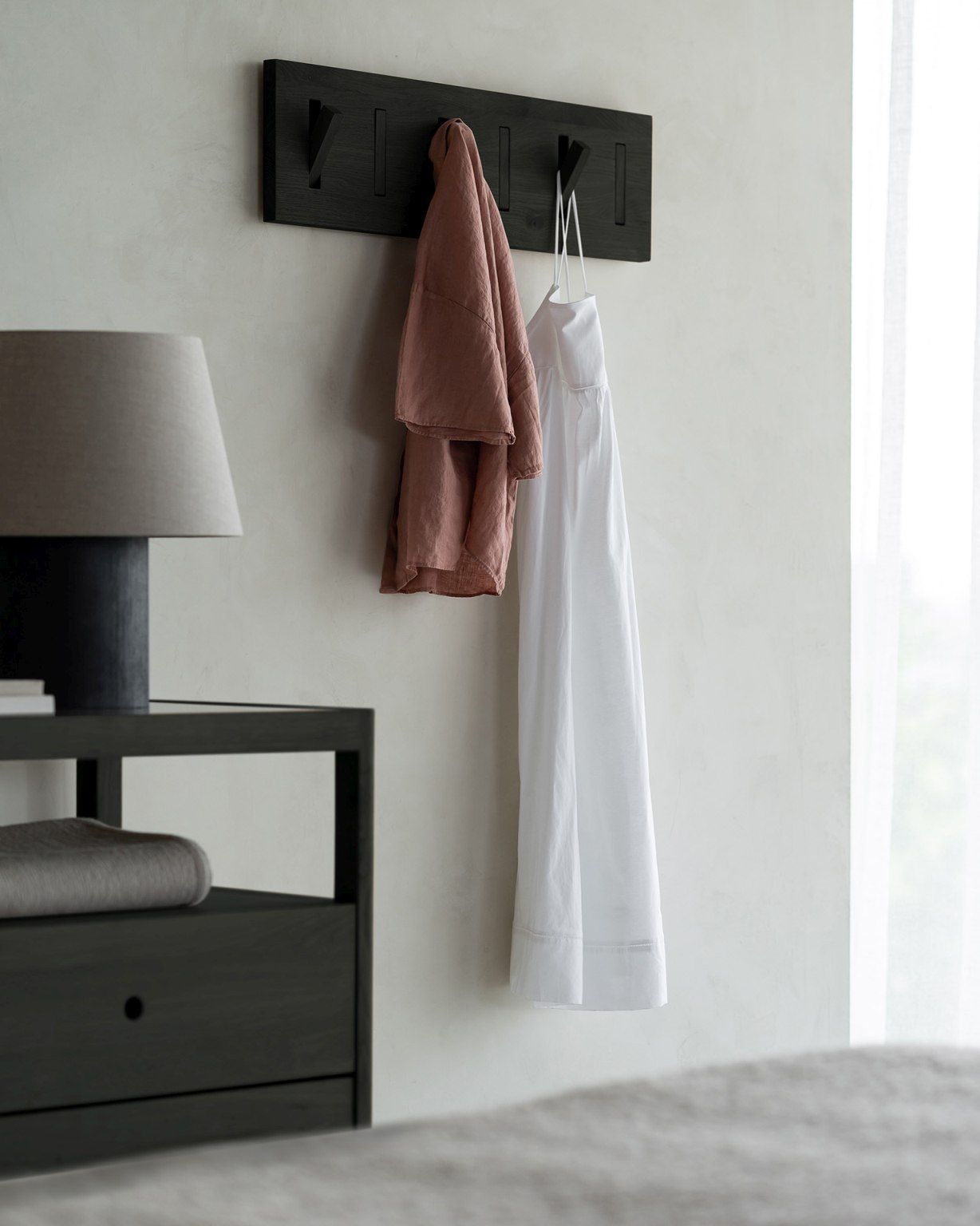 Spindle Kommode mit Schubladen von Ethnicraft, schwarz lackiert, mit Lampe und Kleidung an der Wand.