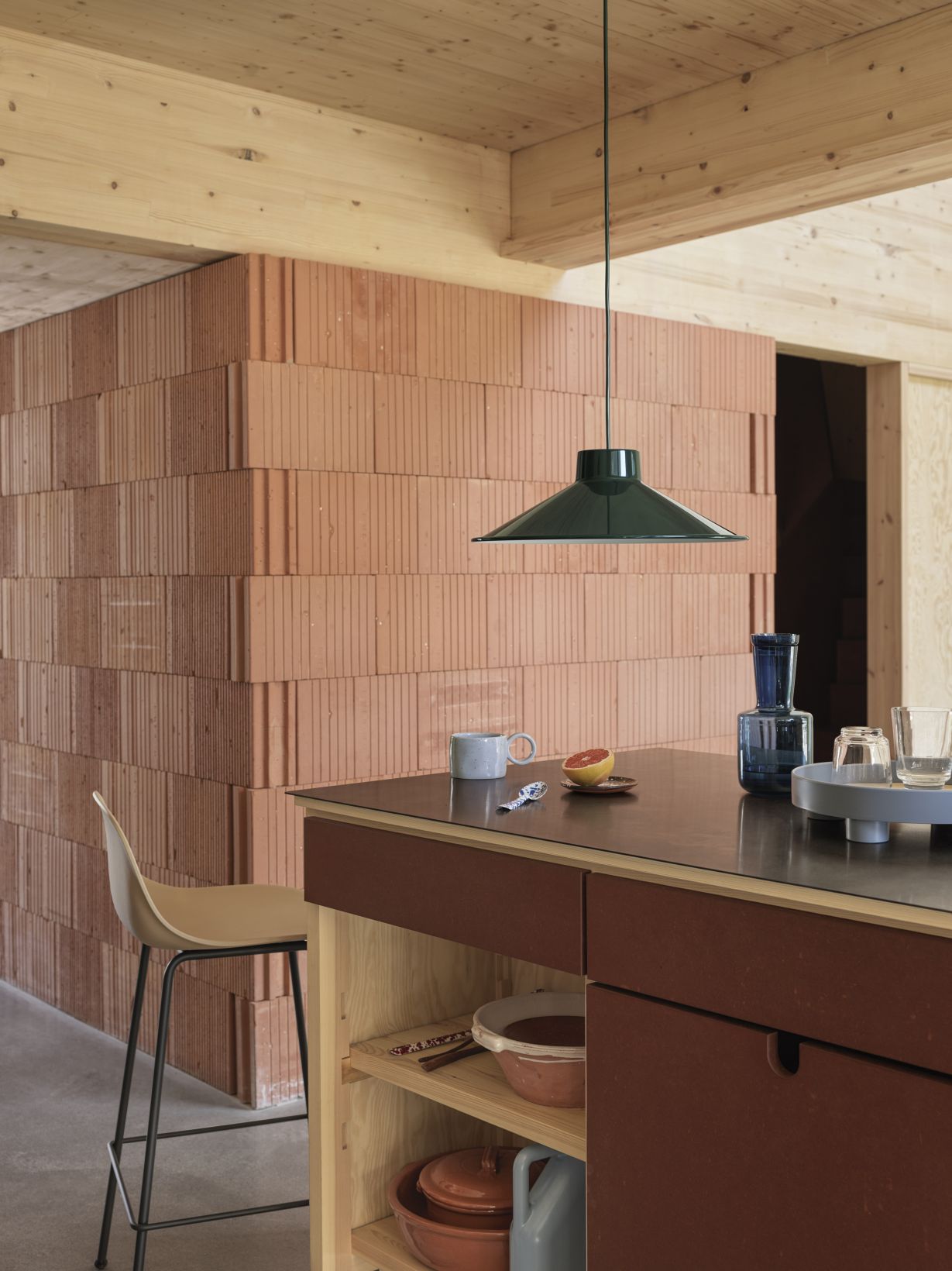 Grüne Muuto Top Pendelleuchte über Küchentisch mit Geschirr und Backutensilien, moderne Innenarchitektur.
