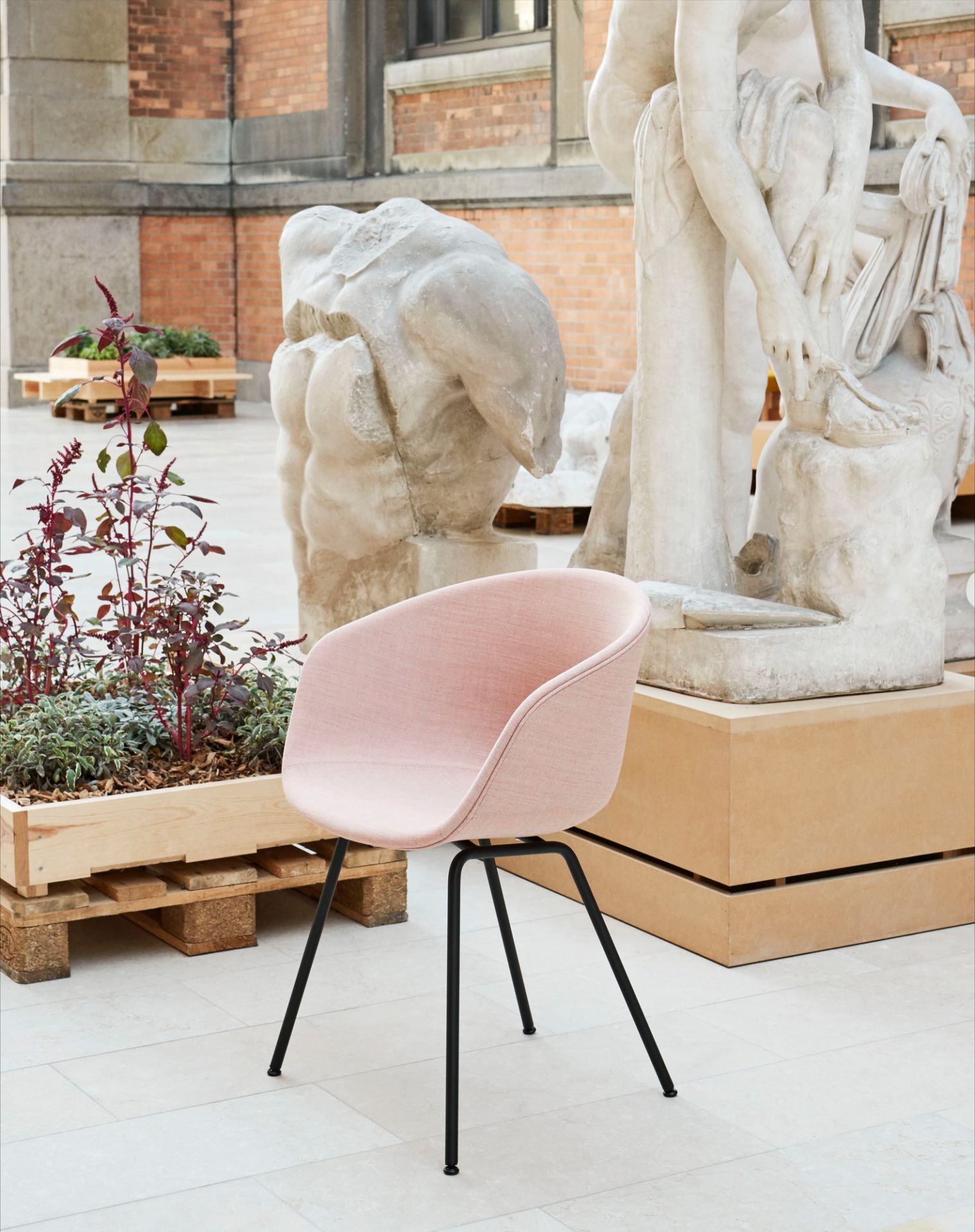About A Chair AAC27 Stuhl in Rosa mit schwarzem Metallfuß vor Statuen im Freien.