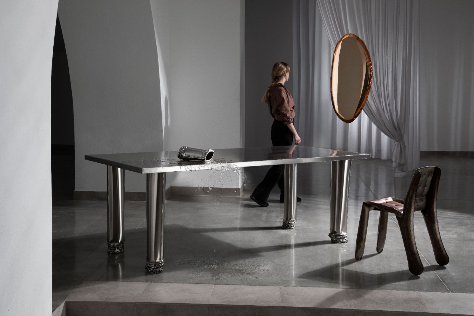 Crash Table Esstisch Zieta aus poliertem Stahl mit Wasser, Stuhl und Frau im Hintergrund.