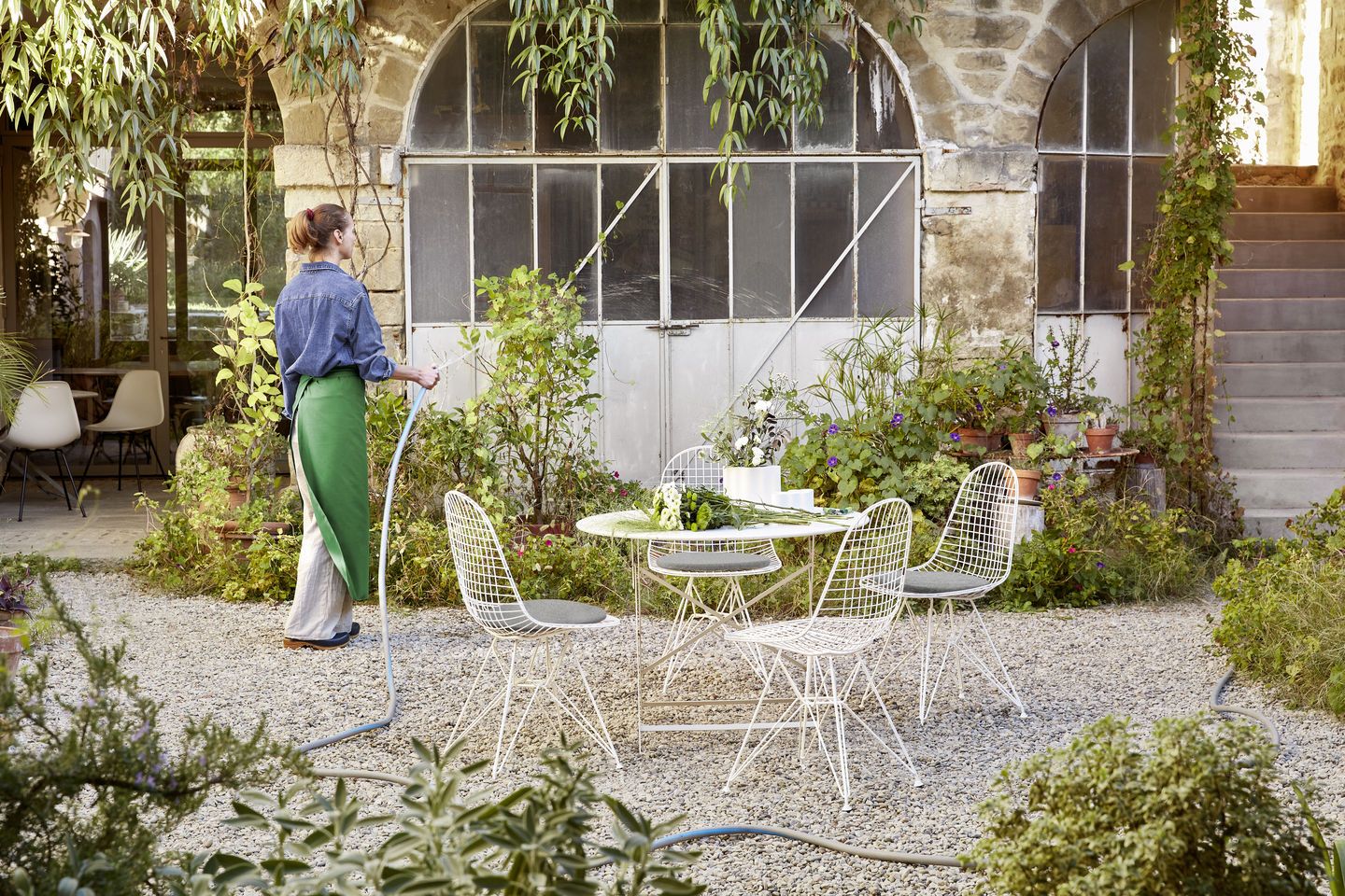 Vitra DKR Wire Chair Stühle mit Sitzkissen in weiß um einen Gartentisch gruppiert.