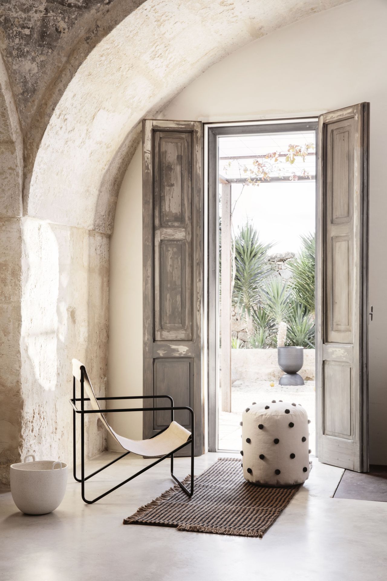 Ferm Living Desert Chair Loungesessel in hellem Raum mit Pouf und Teppich vor geöffneter Tür.