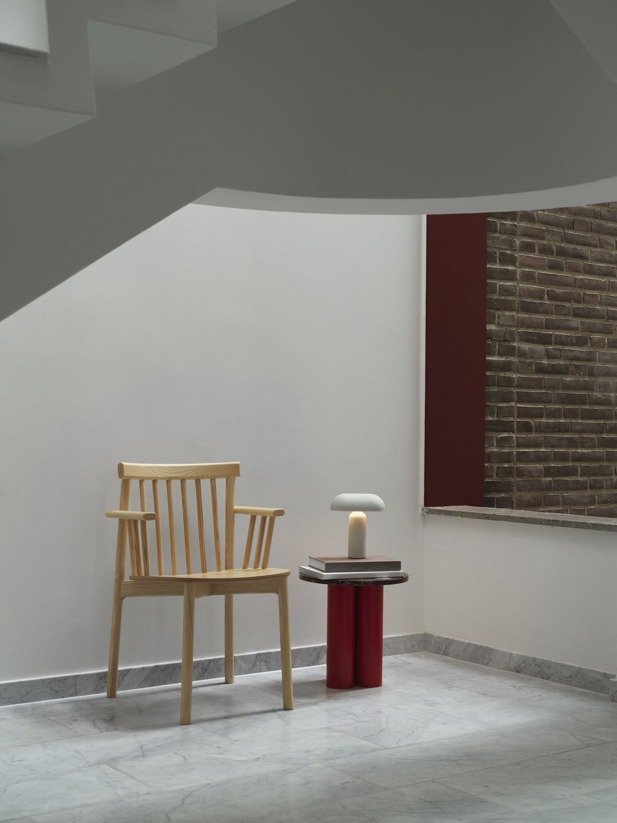 Normann Copenhagen Pind Armchair Armlehnenstuhl aus hellem Holz neben einem kleinen Tisch mit Lampe.